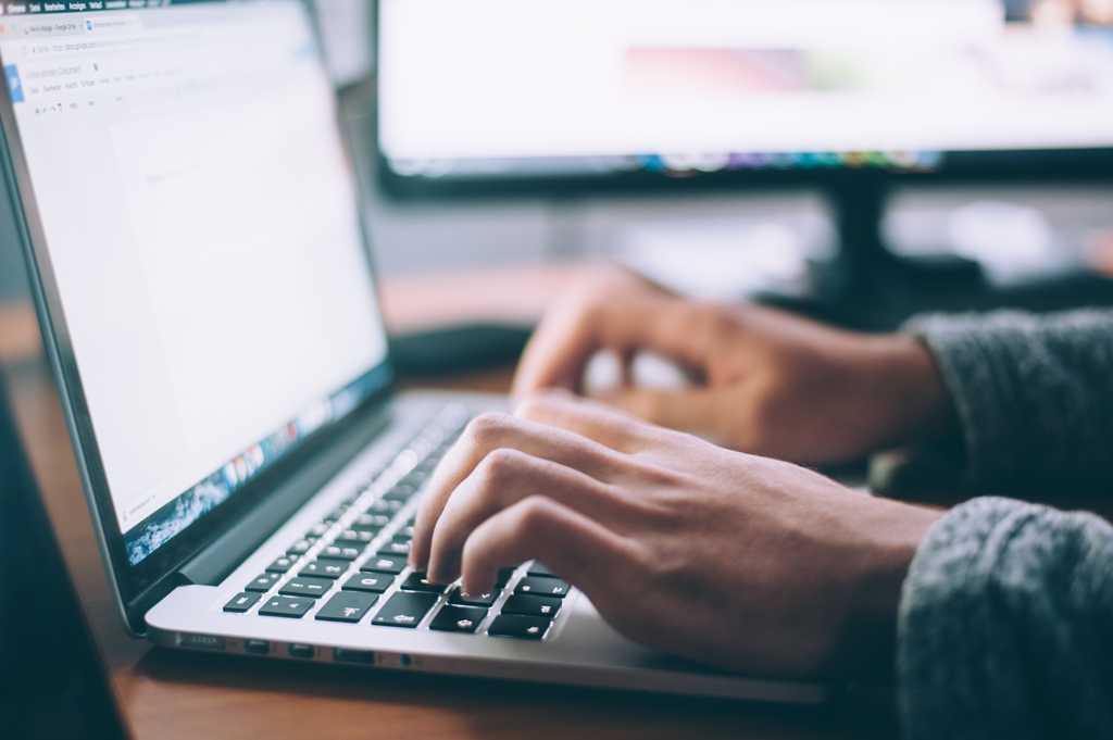 Photo of a person at a laptop writing text within a text editor